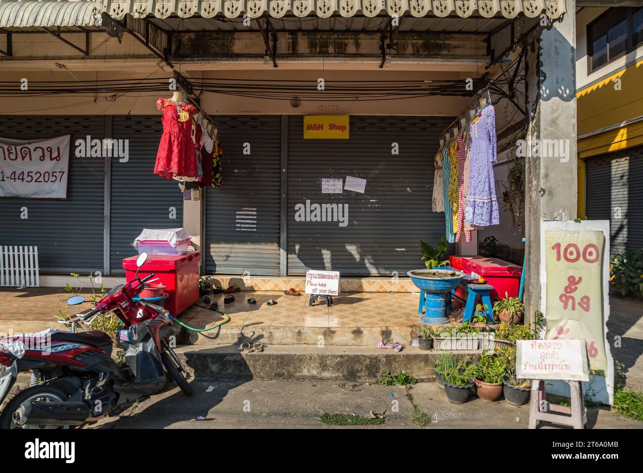 Abiti esposti al negozio di abbigliamento con un cartello che ricorda ai clienti di togliersi le scarpe a Chiang Rai, Thailandia Foto Stock Abiti esposti al negozio di abbigliamento con un cartello che ricorda ai clienti di togliersi le scarpe a Chiang Rai, Thailandia Foto Stock