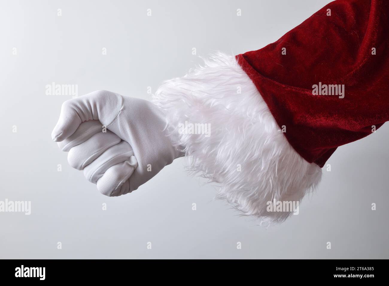 Dettaglio della mano di Babbo Natale con pugno stringato che indossa guanti bianchi tradizionalmente vestiti di rosso isolato con sfondo sfumato dietro. Foto Stock