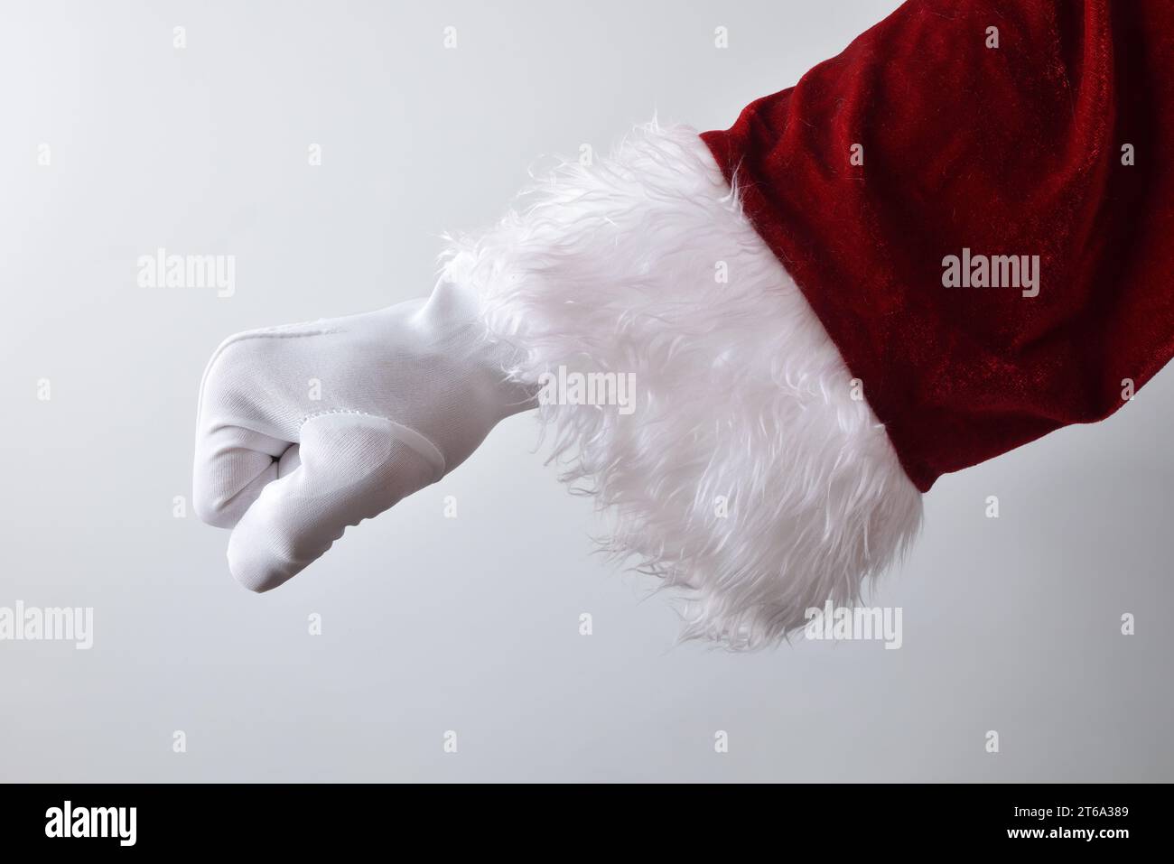 Dettaglio della mano di babbo natale con pugno stringato capovolto nel concetto di impatto con guanti bianchi tradizionalmente vestiti di rosso isolati con sfumatura bac Foto Stock
