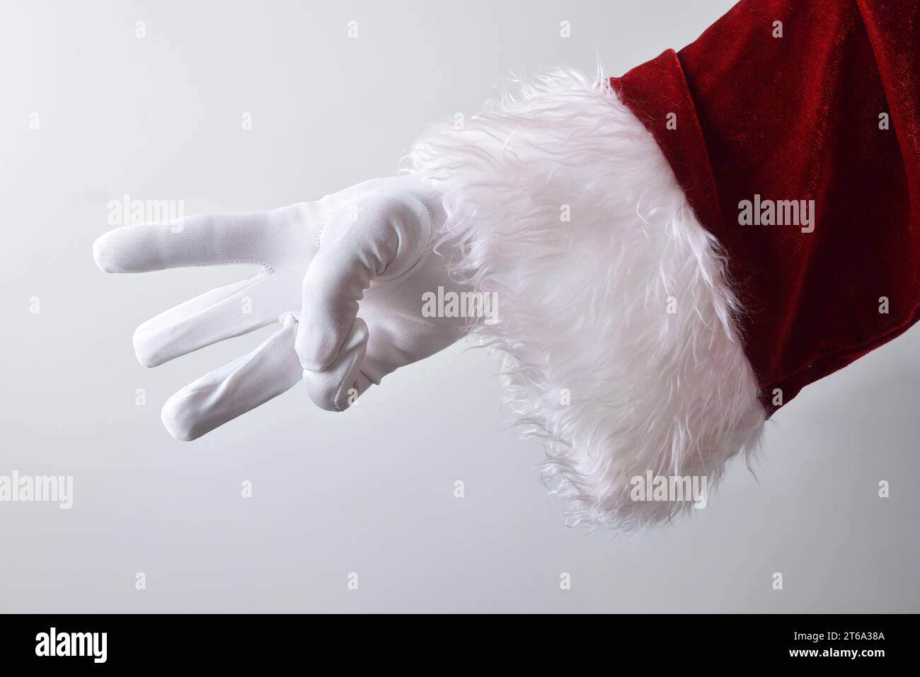 Dettaglio della mano di babbo natale che mostra tre dita con guanti bianchi tradizionalmente vestiti di rosso isolato con sfondo sfumato dietro. Foto Stock