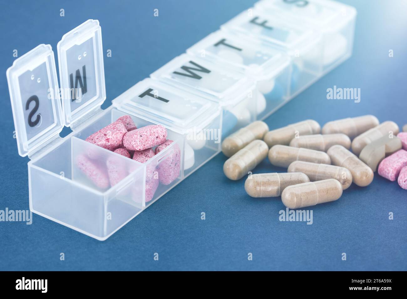 Una settimana di farmaci in una scatola di pillole bianche e accanto in una pila su un tavolo blu. Foto Stock