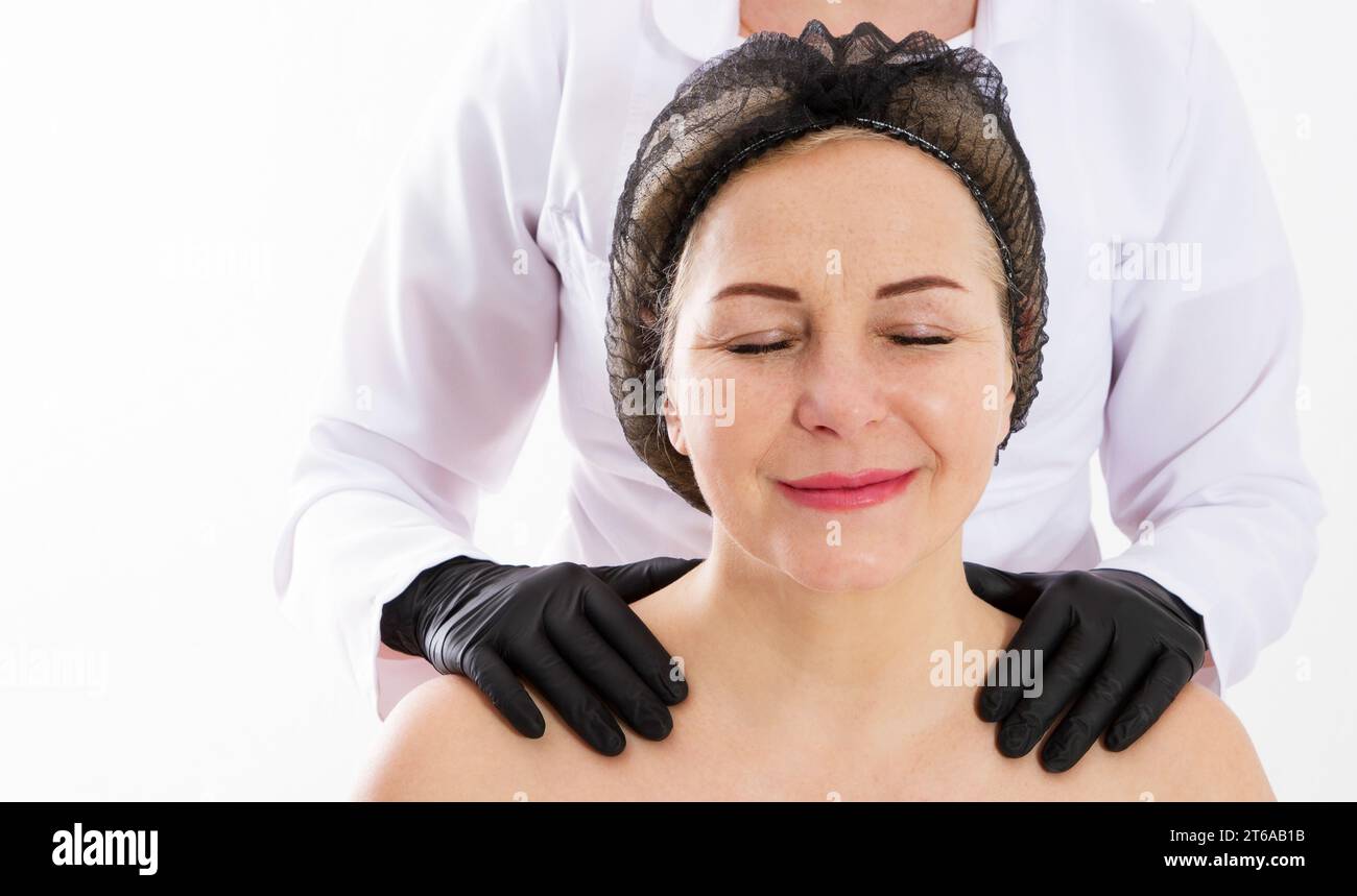 Concetto di invecchiamento e cura della pelle - ritratto di donna di mezza età e le mani di un dermatologo sulle spalle Foto Stock