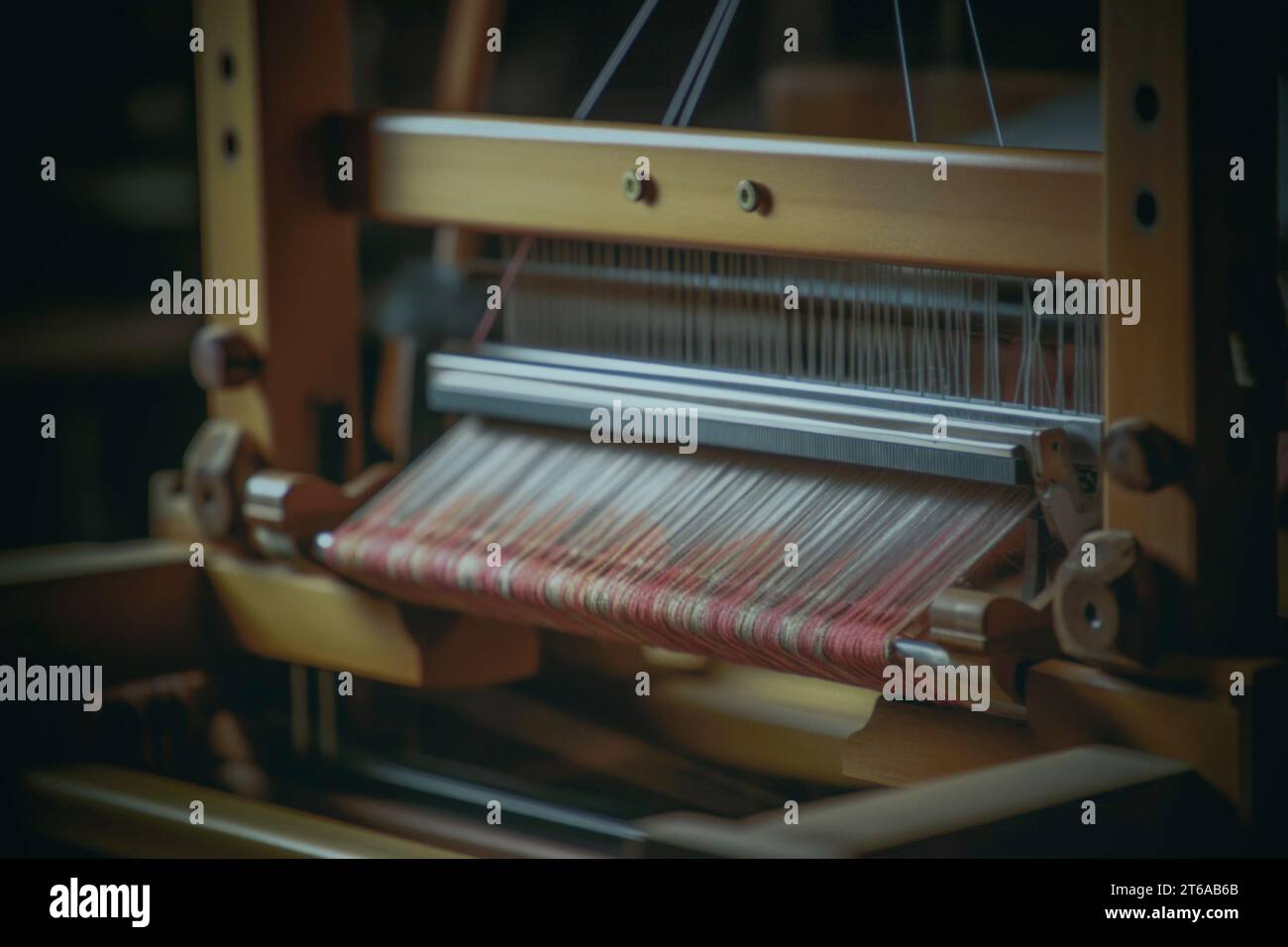 Questa immagine mostra gli intricati dettagli di un telaio a mano artigianale nel processo di tessitura di un tessuto. I toni caldi del legno incorniciano la vivace h Foto Stock