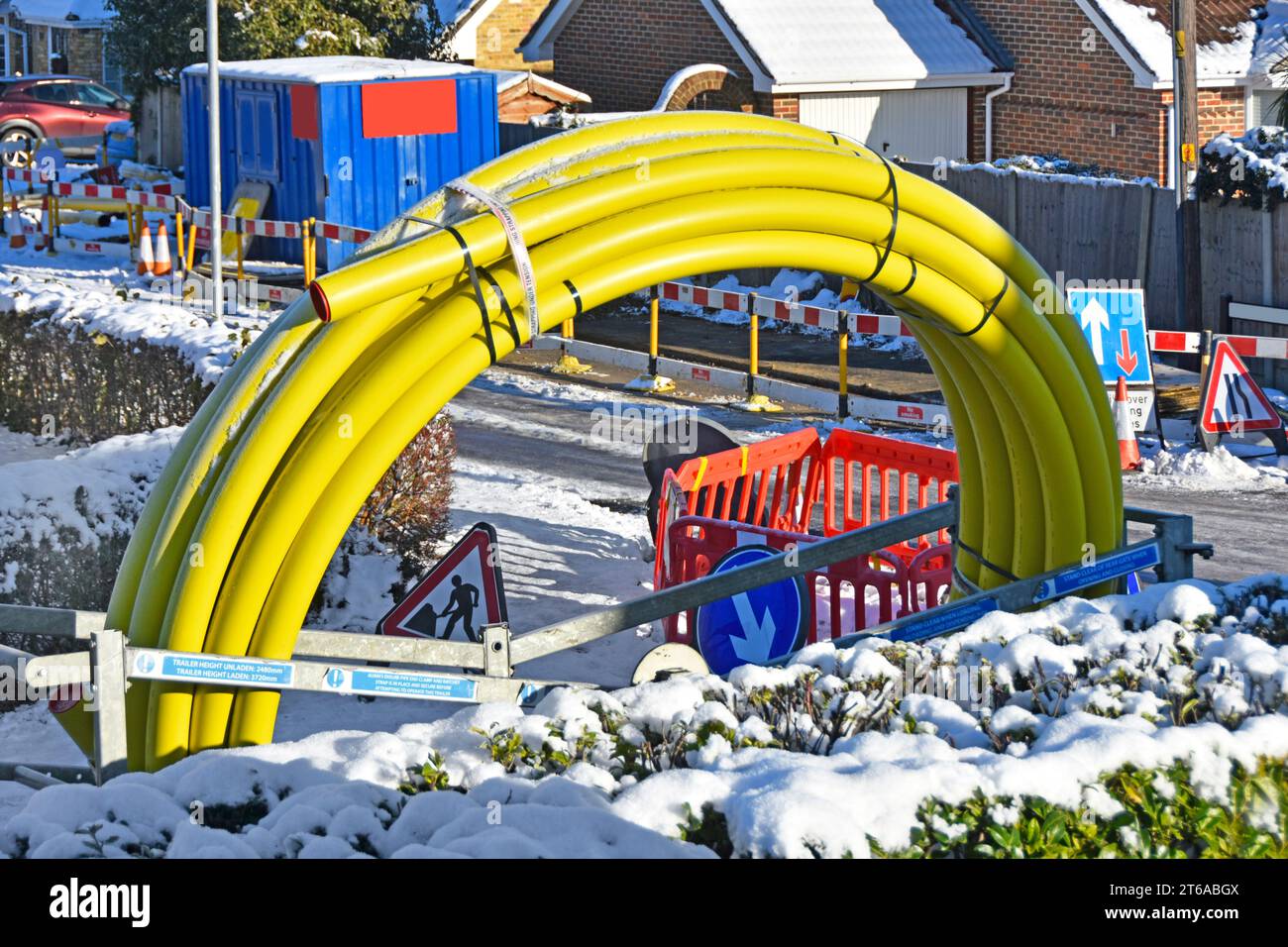 La neve invernale e le strade ghiacciate chiudono i lavori stradali in un villaggio residenziale, il grande tubo principale a spirale del gas giallo, in sostituzione della ghisa Essex England UK, che invecchia Foto Stock