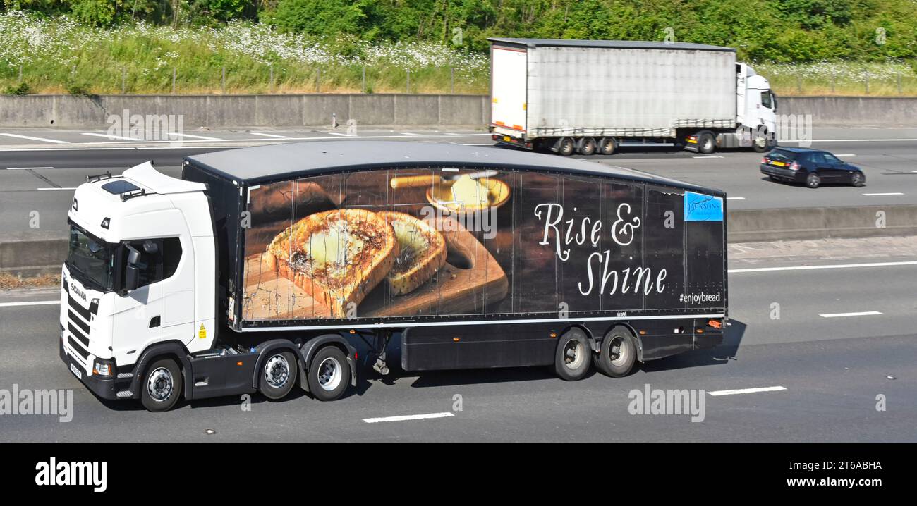 Le unità autocarri articolati hgv sulla carreggiata opposta e direzione sull'autostrada M25, una bianca senza contrassegno, confrontano la pubblicità elaborata Rise & Shine UK Foto Stock