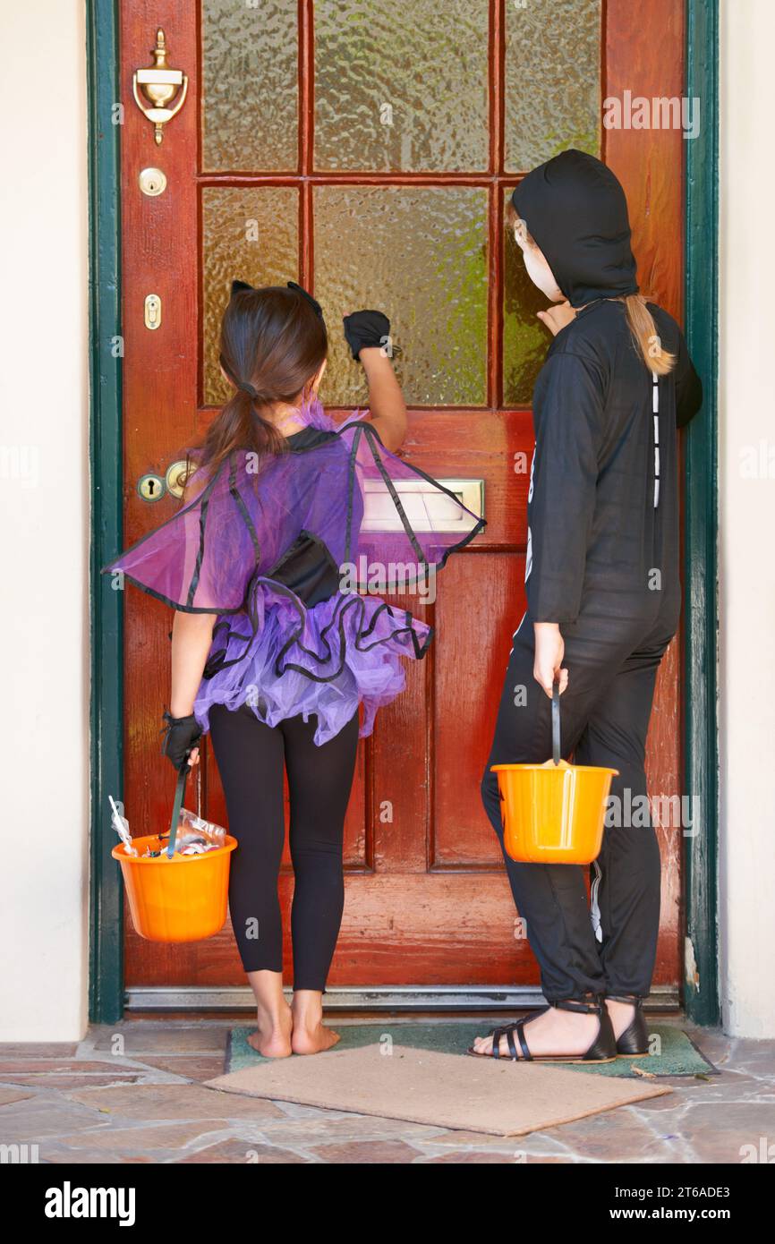 Zecche o trattamento è molto divertente. Foto retrovisiva di alcuni bambini che bussano a una porta durante halloween. Foto Stock