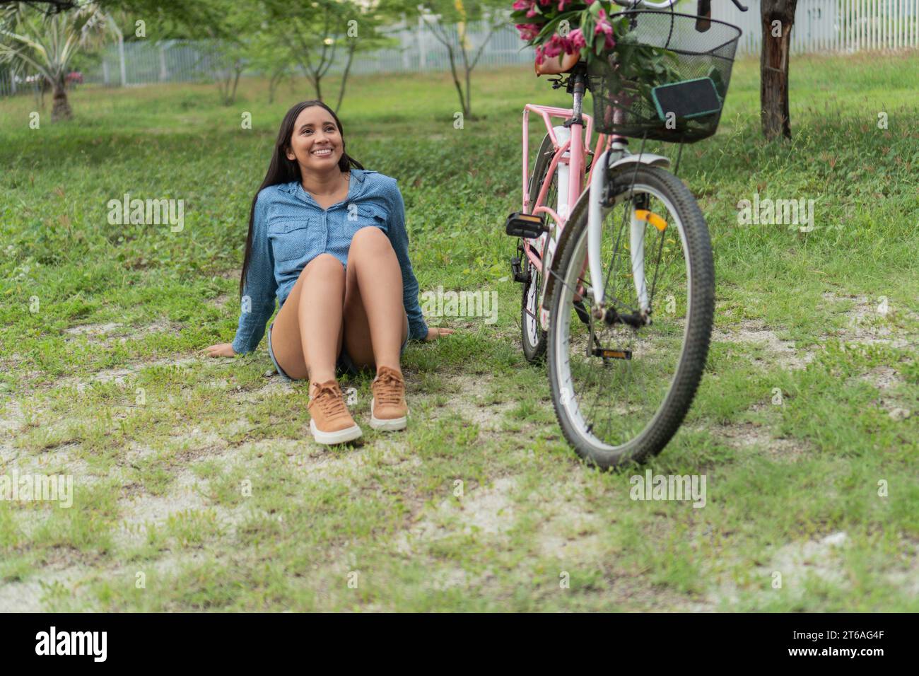 Donna latina seduta accanto a una bicicletta con fiori nel cestino. Foto Stock