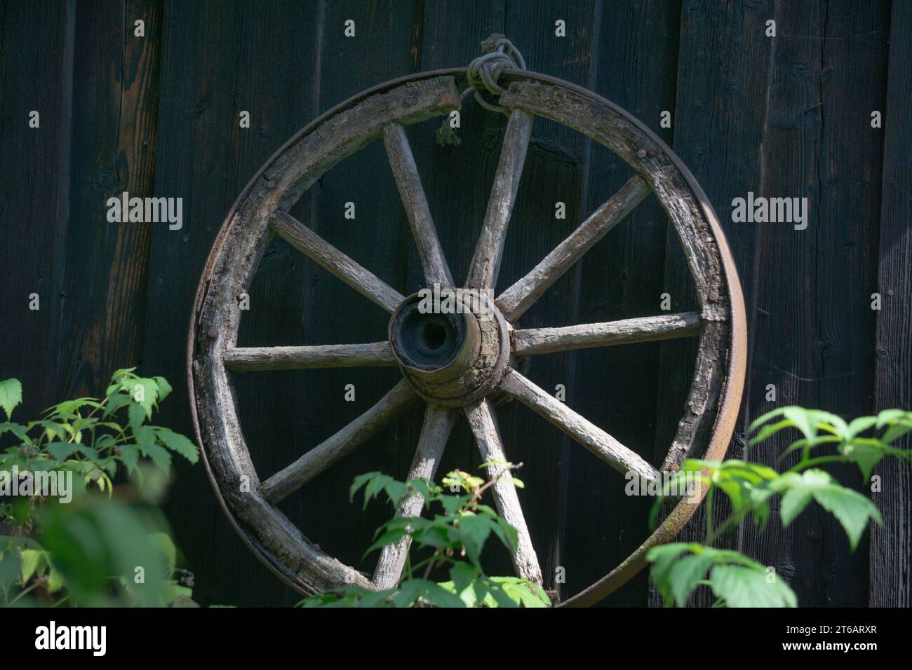 Una vecchia ruota di legno in una treccia di ferro sulla parete di una casa Foto Stock