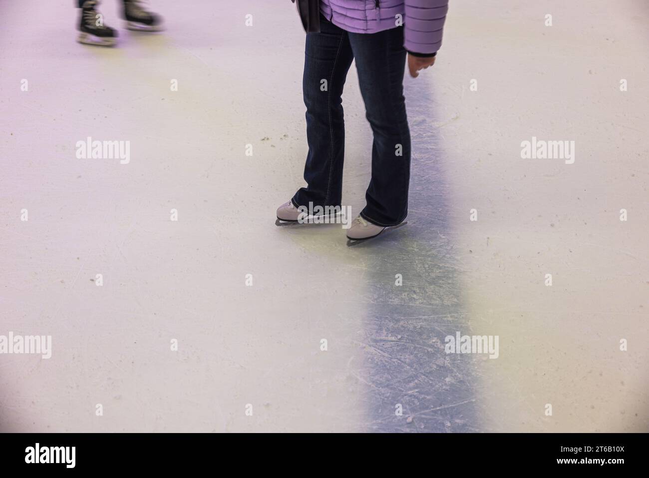 Vista ravvicinata delle gambe delle donne in jeans che indossano pattini bianchi sulla pista di pattinaggio su ghiaccio nel complesso sportivo. Foto Stock