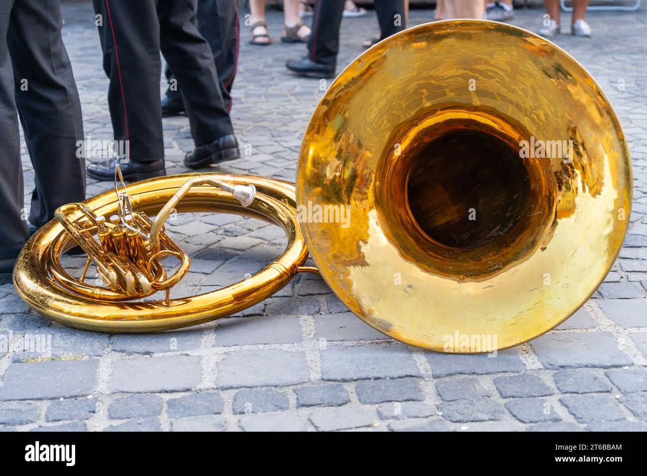 Tuba di ottone che giace per terra in una strada acciottolata con musicisti soldato sullo sfondo Foto Stock