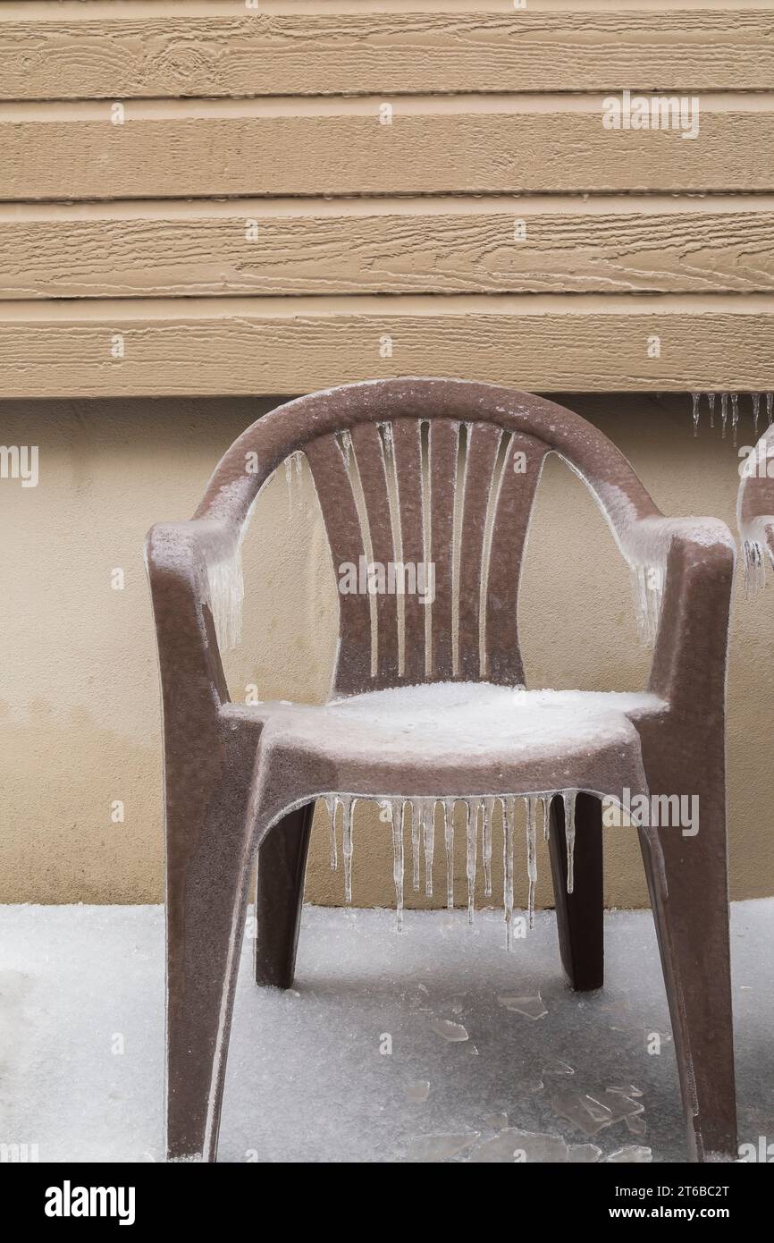 Poltrona da giardino in plastica marrone coperta di ghiaccio e neve accanto al muro della casa. Foto Stock