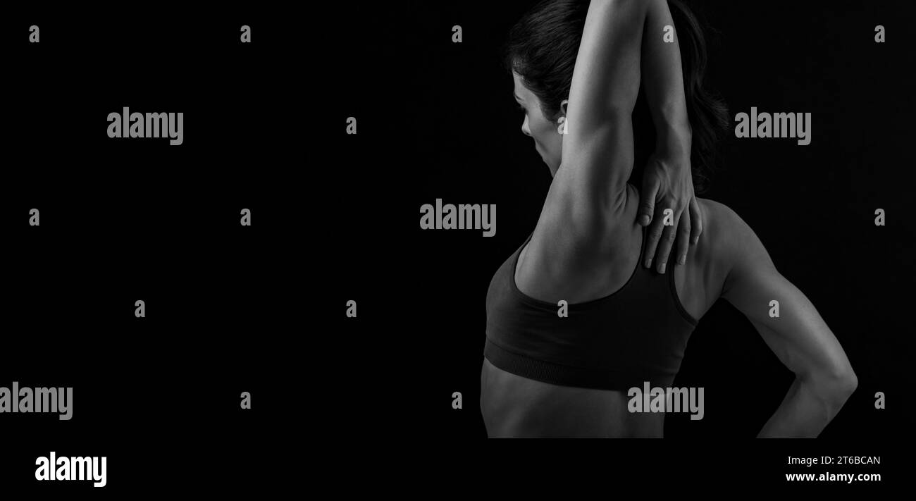 Donna sportiva e muscolosa che fa stretching rilassante allenamento delle spalle, lame nel reggiseno sportivo, tenendo il collo alla mano sullo schienale nero dello studio Foto Stock