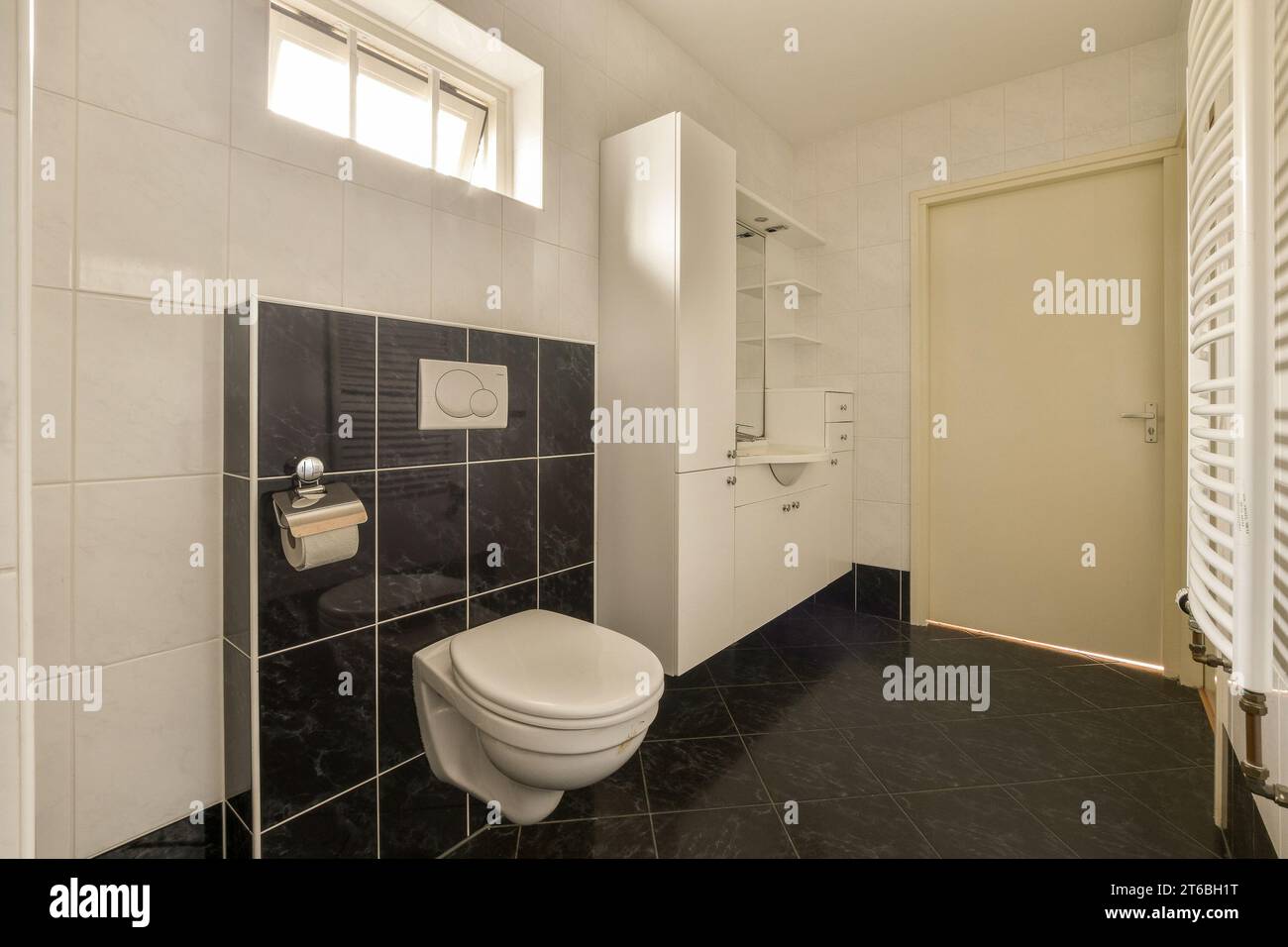 bagno con piastrelle bianche e nere alle pareti, rotoli di carta igienica davanti alla porta della camera Foto Stock