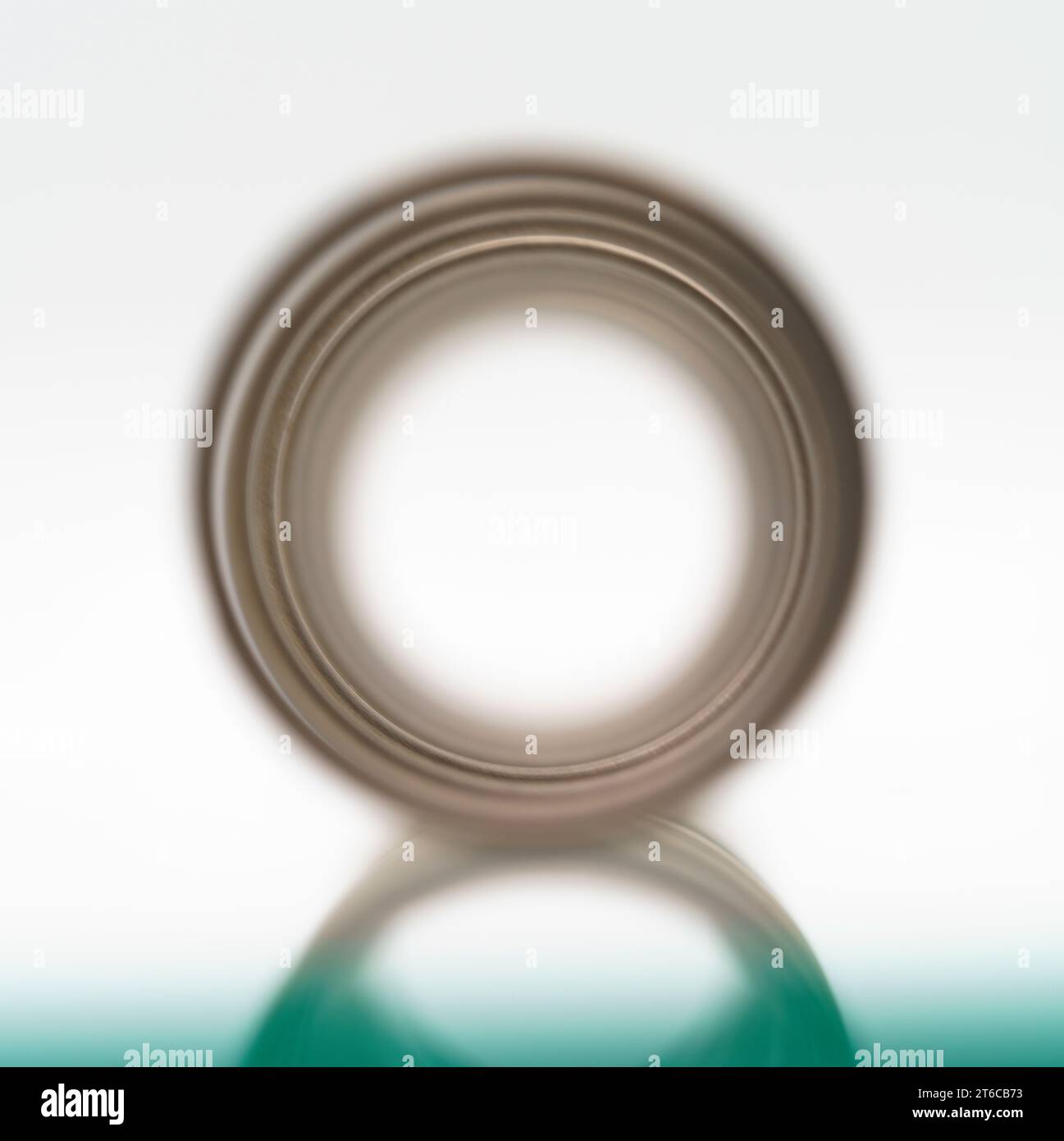 Una vista macro del centro tubolare di una molla e il suo riflesso giacente su un foglio di vetro Foto Stock