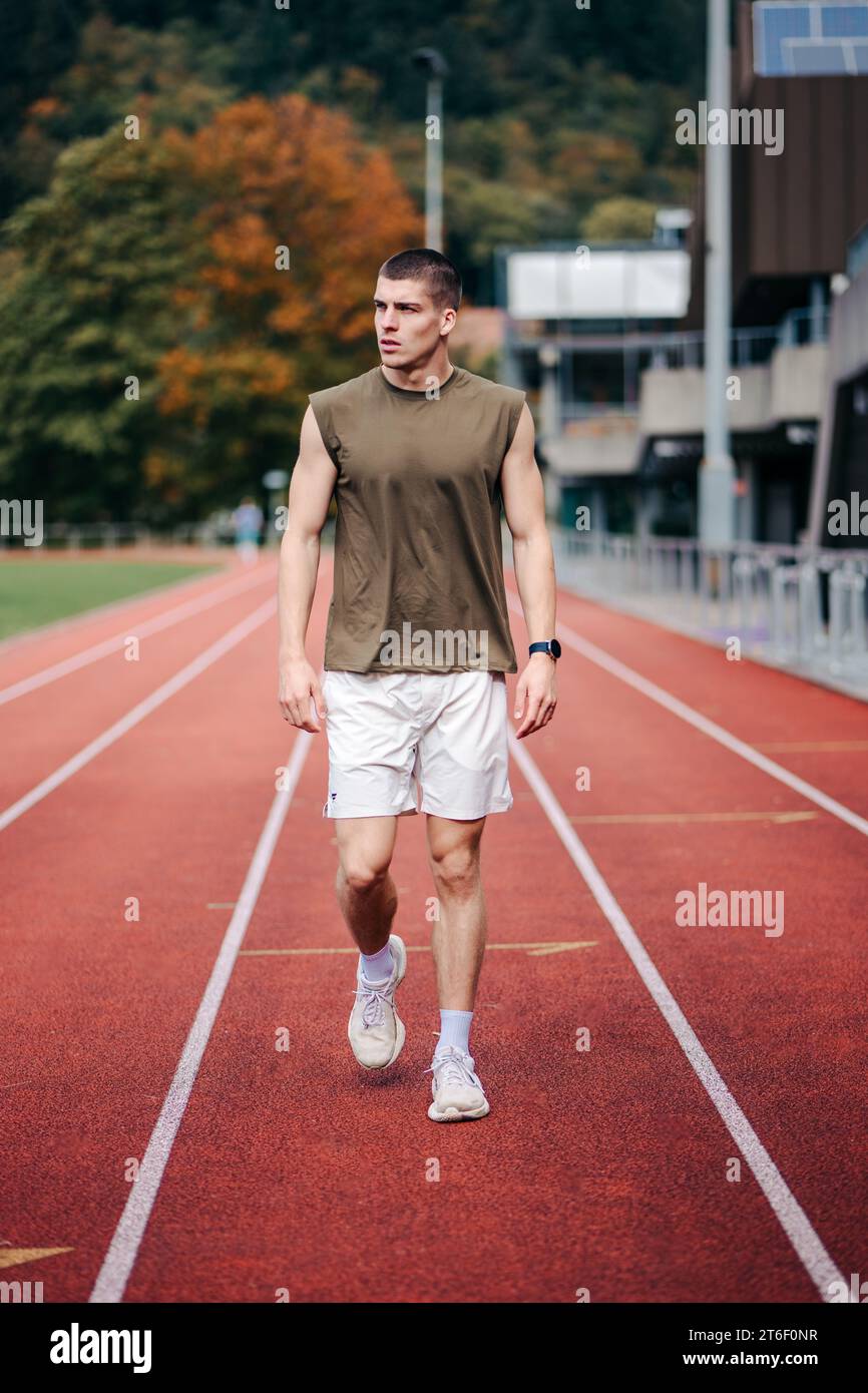 Una figura maschile che corre con sicurezza su una pista da corsa arancione in un ambiente da stadio Foto Stock