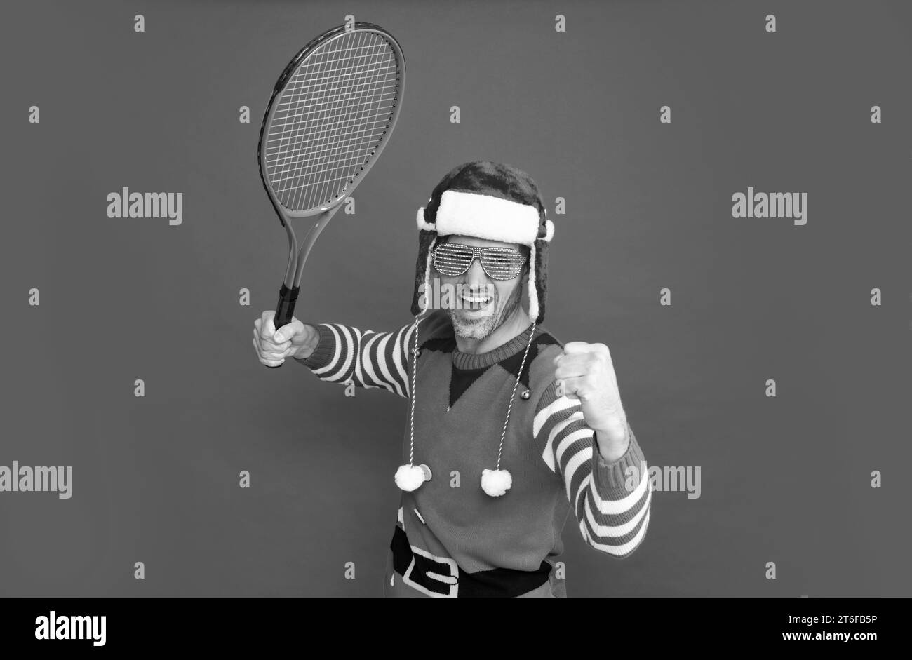 felice uomo di successo in costume di elfo e cappello di babbo natale. il ragazzo di natale tiene il razzo di tennis Foto Stock