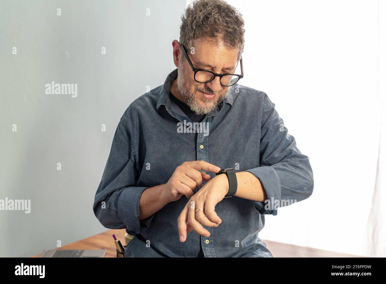 Un uomo di mezza età con capelli grigi e occhiali sorridente mentre interagisce con il suo smartwatch, mostrando l'integrazione della moderna tecnologia indossabile in Foto Stock