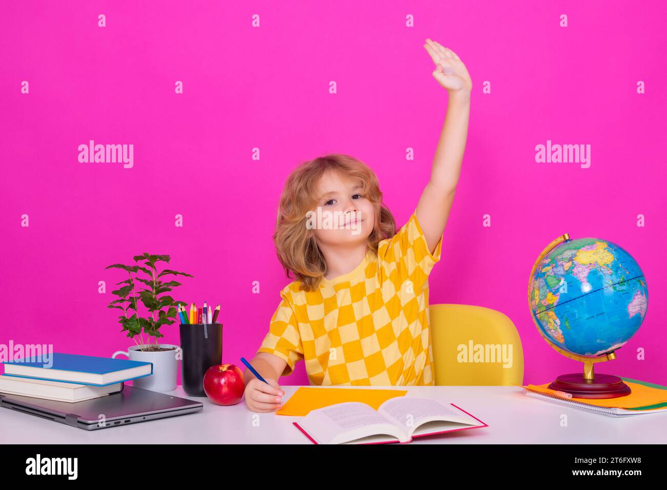 Bambino della scuola che alza la mano, disposto a rispondere alle domande. Il ragazzo della scuola nerd isolato sullo sfondo dello studio. Bambino intelligente della scuola elementare con il libro. Foto Stock