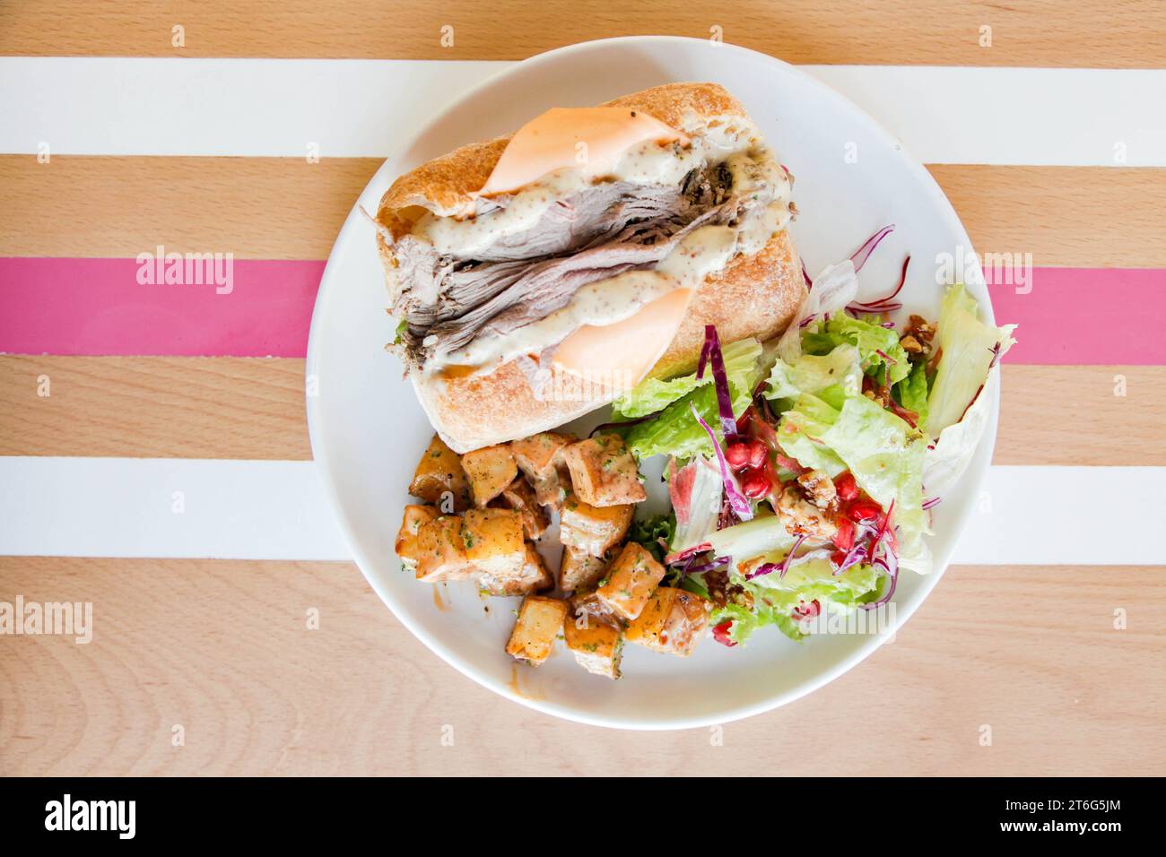 Panino aperto di roast beef su un piatto servito con verdure sul lato su un tavolo di legno con strisce. Foto Stock