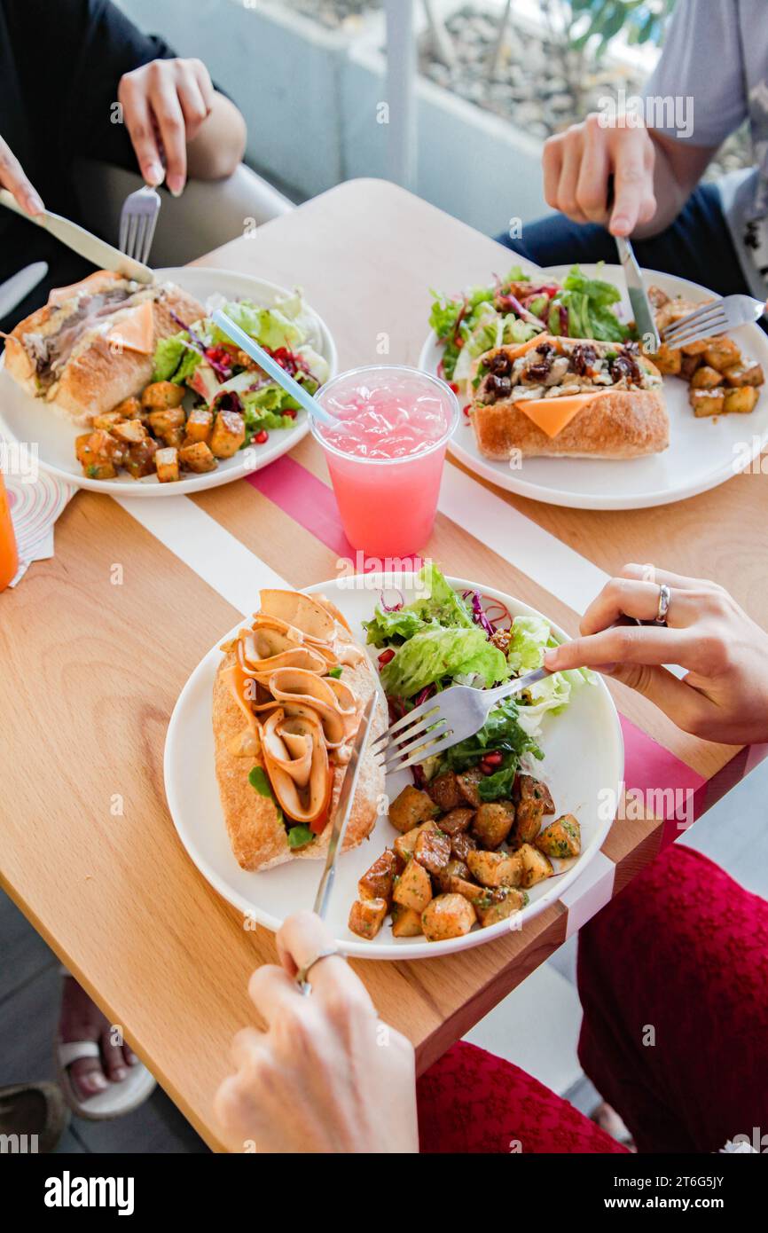 Tre persone che hanno un cibo informale si incontrano gustando sanwiches e fast food a pranzo. Foto Stock