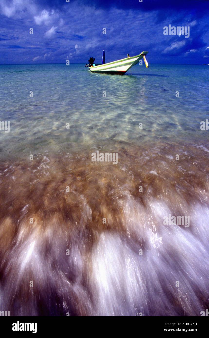 Una vista ad ampio angolo di una barca a coda lunga, con onde che si infrangono sulla spiaggia in primo piano, Koh Phangan. Foto Stock