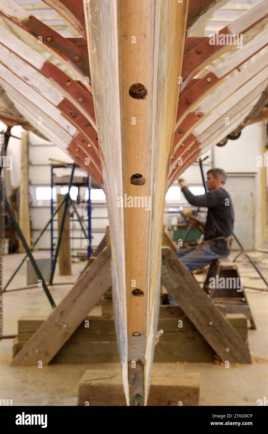 Un uomo lavora per restaurare una barca a vela di legno a Warren, Maine. Foto Stock