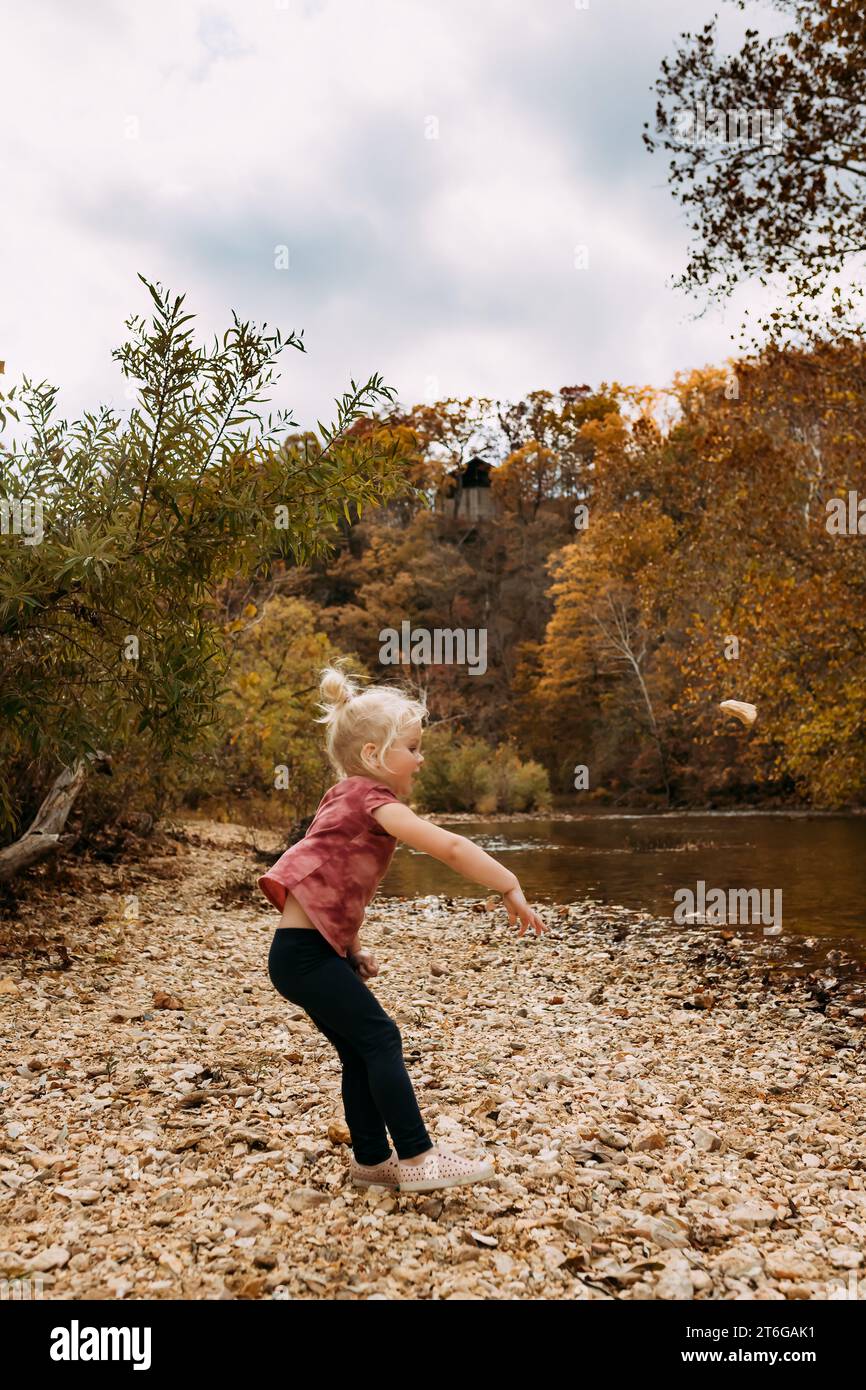 Bambini che gettano rocce nel fiume durante il giorno d'autunno Foto Stock
