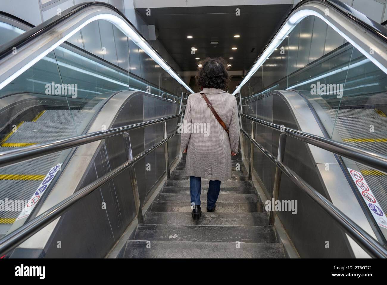 Donna da dietro scala in discesa tra scale mobili per allenarsi, metro, metropolitana, Spagna. Foto Stock