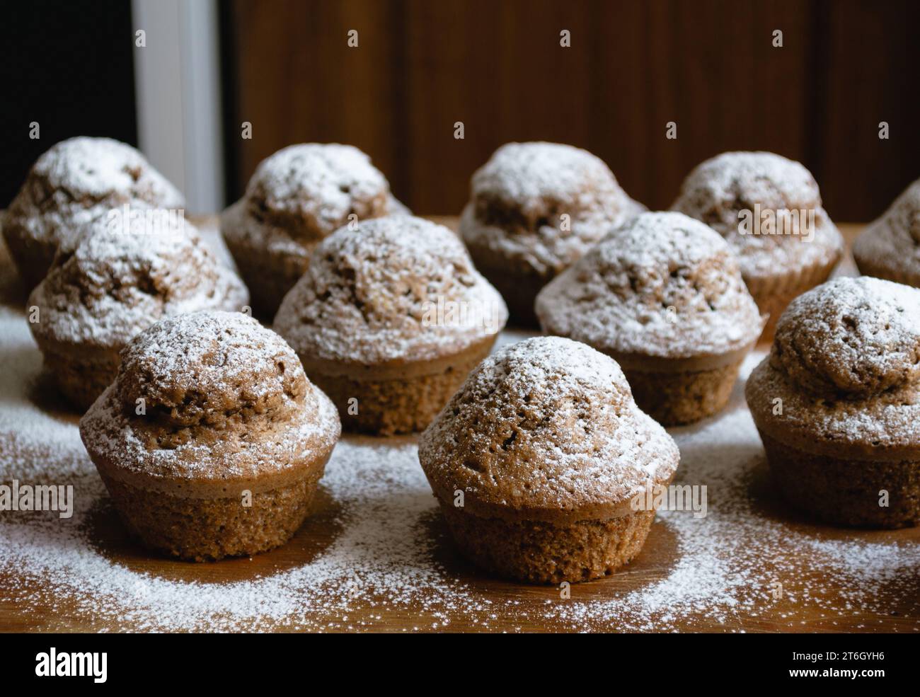 Primo piano di deliziosi cupcake al cioccolato al forno su una tavola di legno e cosparsi di zucchero bianco in polvere Foto Stock