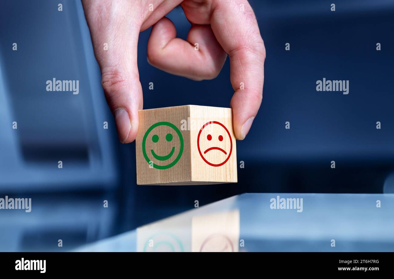 La mano ruota il cubo di legno e cambia l'espressione di un sorriso. Foto Stock