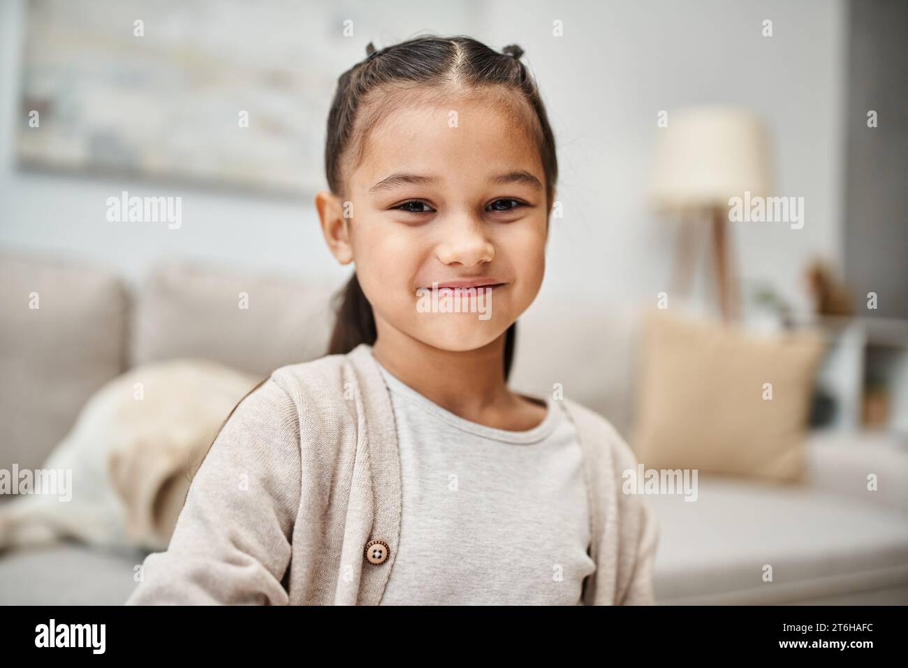 ritratto di una ragazza felice dell'età elementare con i capelli bruna sorridenti davanti alla macchina fotografica in un appartamento moderno Foto Stock