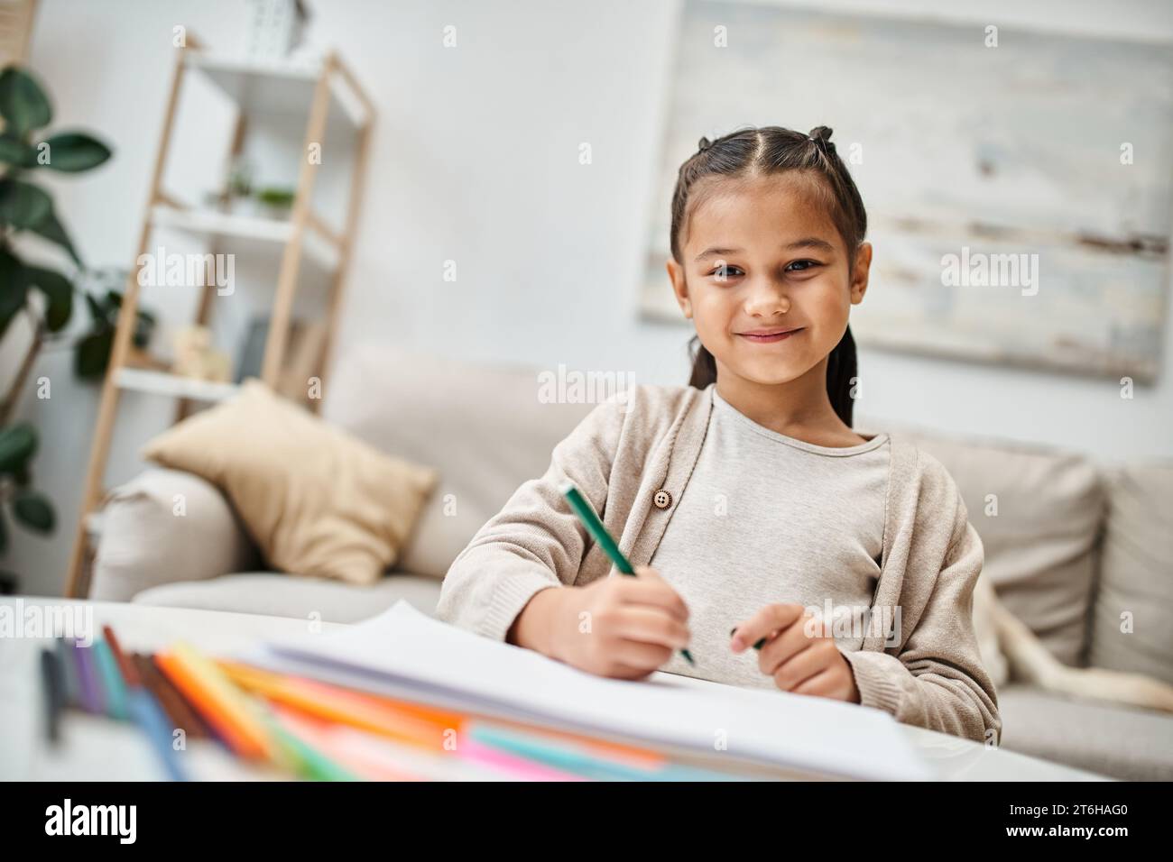 ritratto di una ragazza dell'età elementare felice che disegna con matita colorata e sorride in un appartamento moderno Foto Stock