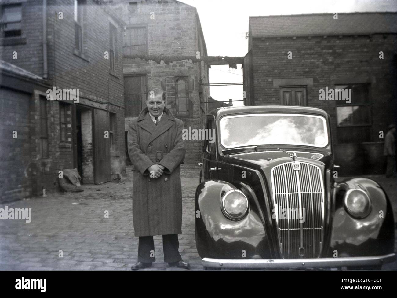 1950, storico, in un cortile acciottolato con magazzini circostanti, un gentiluomo in piedi con orgoglio vicino alla sua auto dell'epoca, forse un Rover di produzione britannica, Inghilterra, Regno Unito. Foto Stock