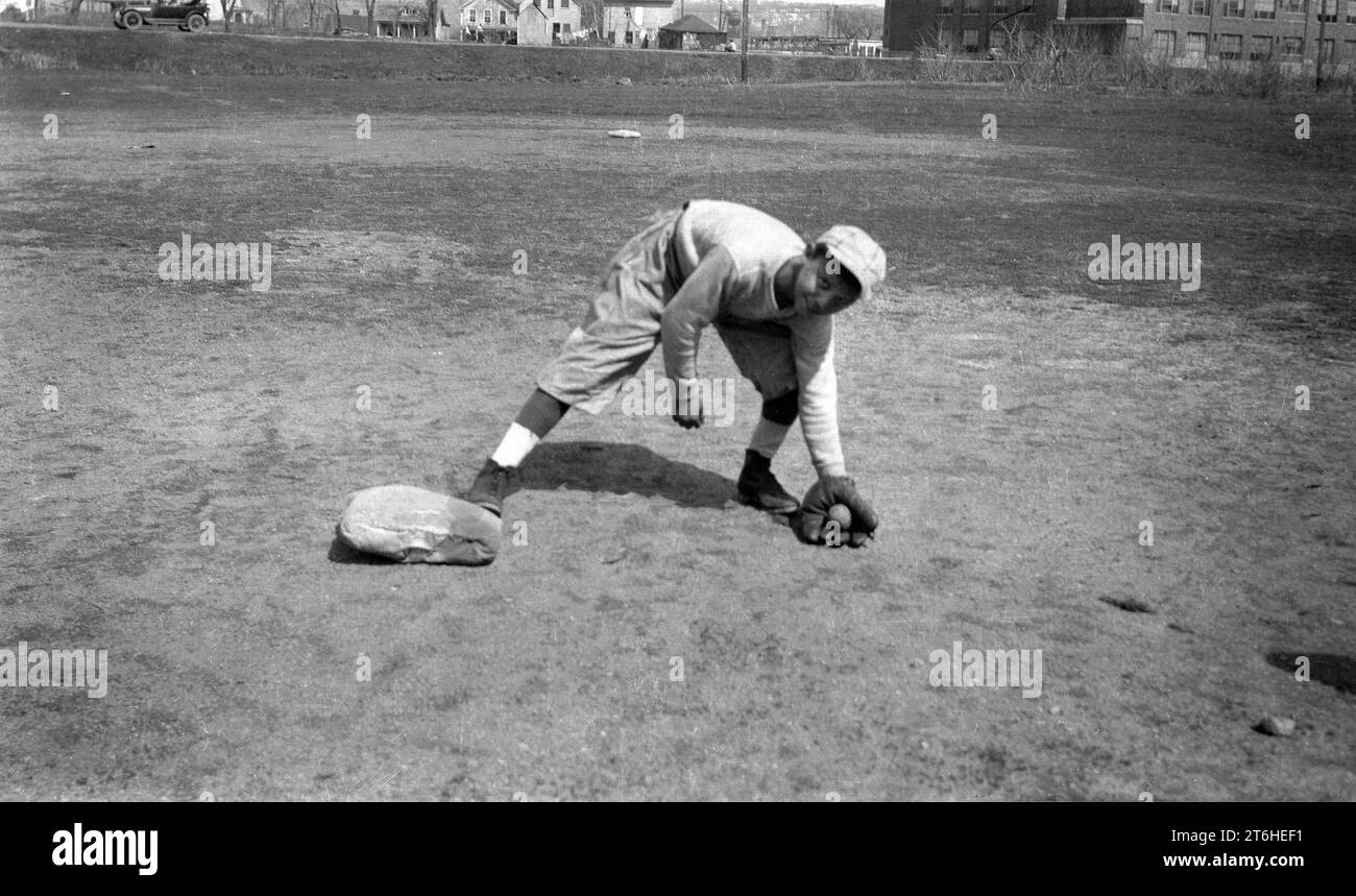 1934, storico, all'esterno dei terreni della Mapplewood Grammar School, un ragazzo che indossa una divisa da baseball e un guanto o un guanto da baseball nella mano sinistra mentre gioca una palla in una base, Stati Uniti Foto Stock