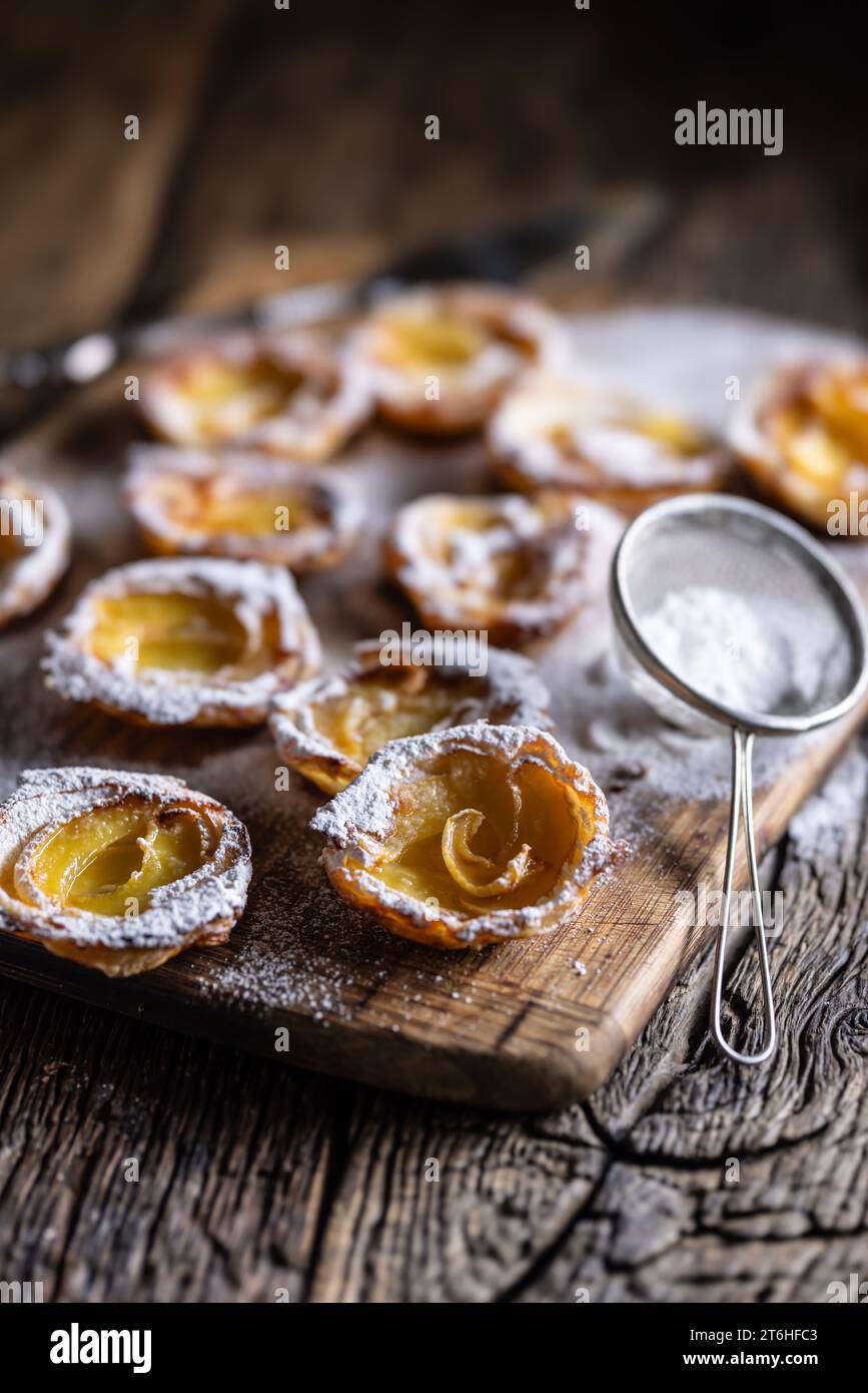 Mini crostate di pasta sfoglia e mele a fette cosparse di zucchero in polvere su tagliere di legno. Dolci di mele francesi - primo piano. Foto Stock