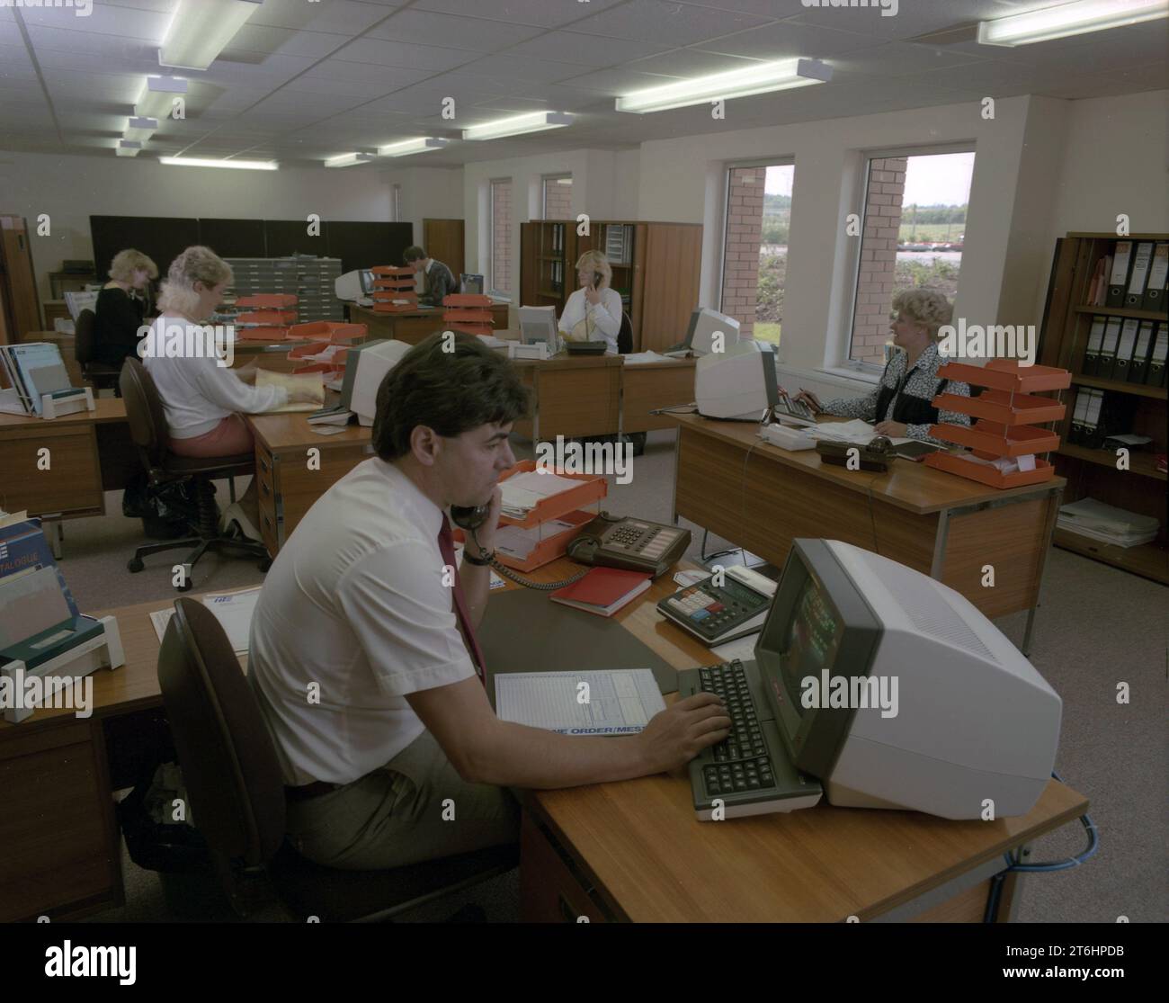 Alla fine degli anni '1980, ufficio open space, dipendenti di una società di forniture elettriche che lavorano alle scrivanie utilizzando monitor per computer dell'epoca, Inghilterra Regno Unito. Dipendente al telefono che guarda lo schermo del monitor con un blocco ordini sulla scrivania. Foto Stock