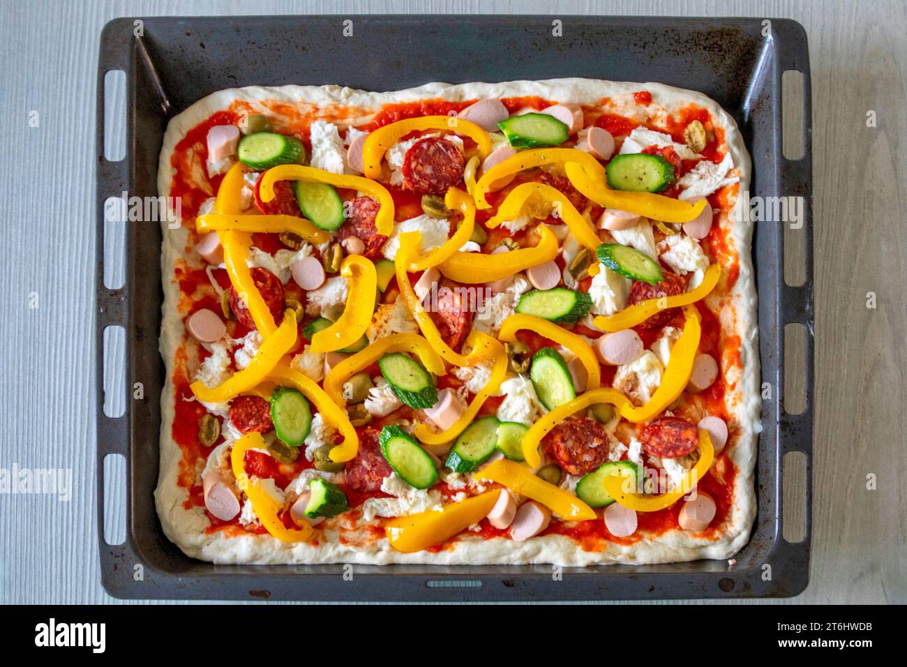 Pizza italiana fatta in casa prima di essere cotta in forno, ripiena di pomodoro, mozzarella, peperoni, zucchine, frankfurters e salame piccante Foto Stock