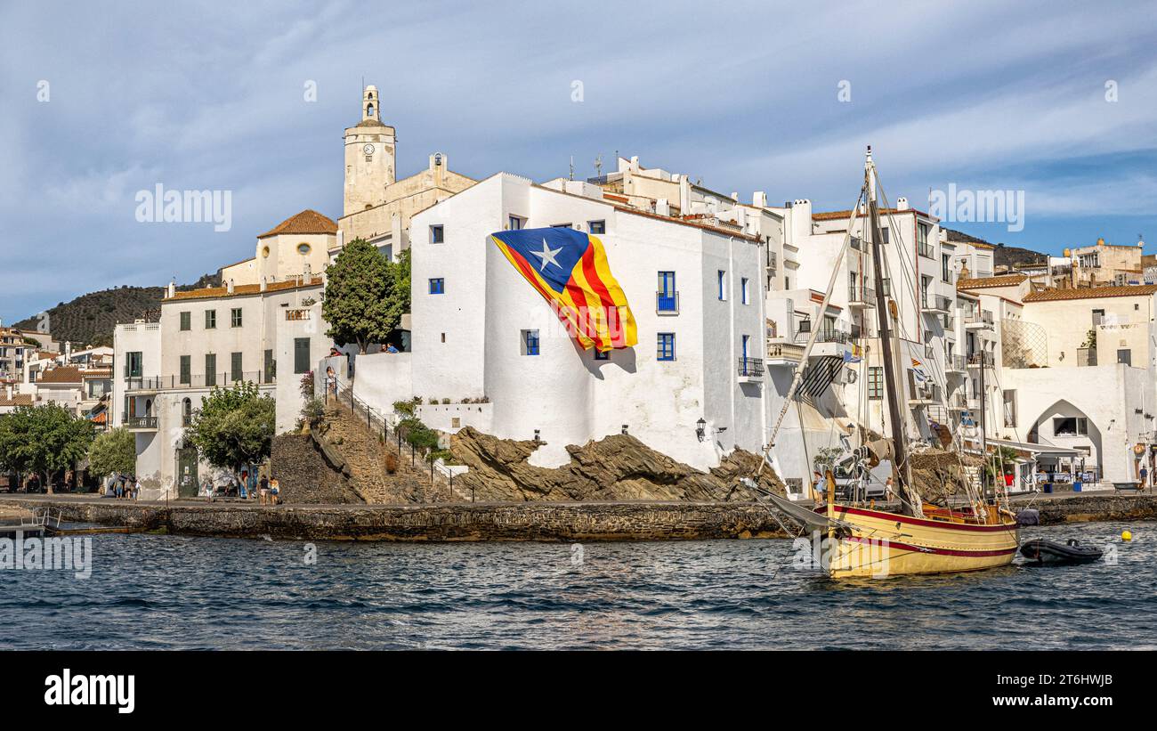 Città vecchia con bandiera catalana e barca a vela. Cadaques, Catalogna, Spagna. Foto Stock