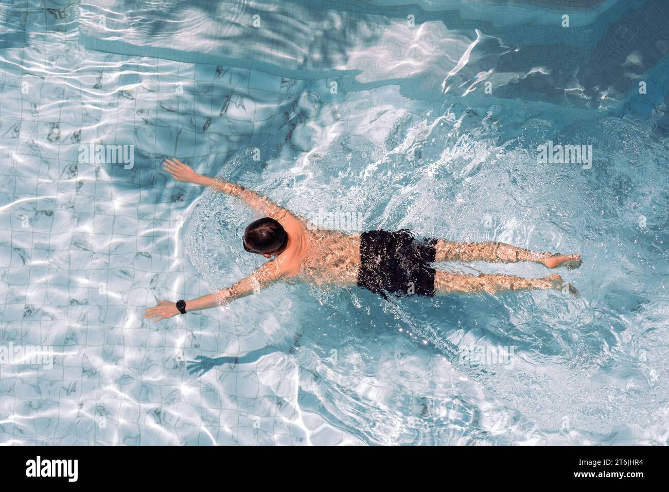 Un adulto maschio che nuota in una piscina coperta con un orologio intelligente Foto Stock