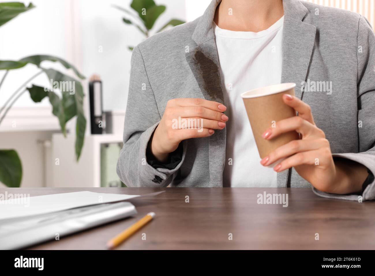 Donna che mostra macchie di caffè sulla giacca al tavolo di legno all'interno, primo piano Foto Stock