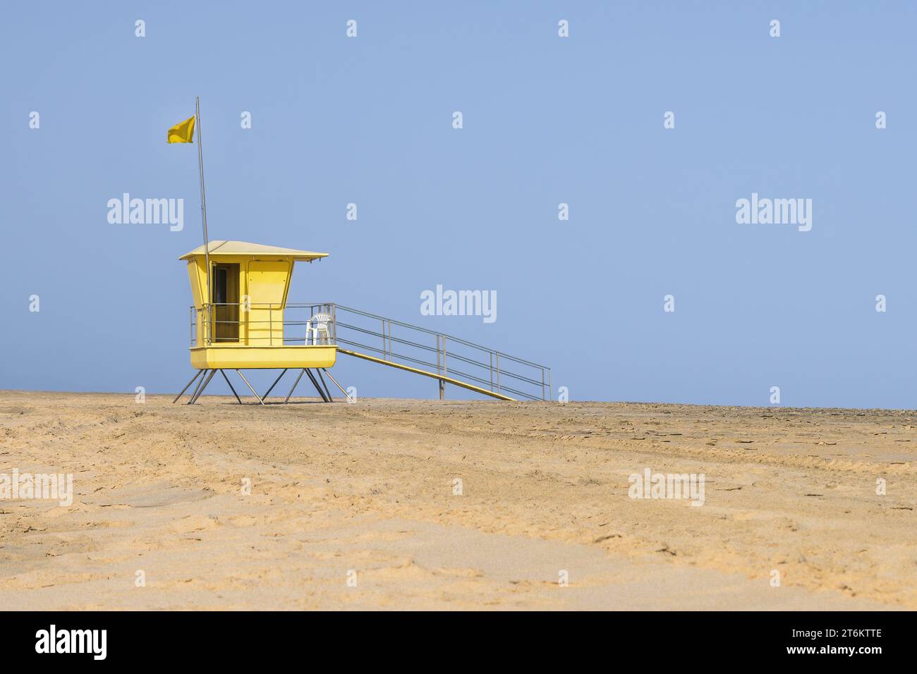 La torre gialla del bagnino sulla spiaggia con bandiera gialla di sicurezza davanti al cielo blu. Copia spazio. Foto Stock