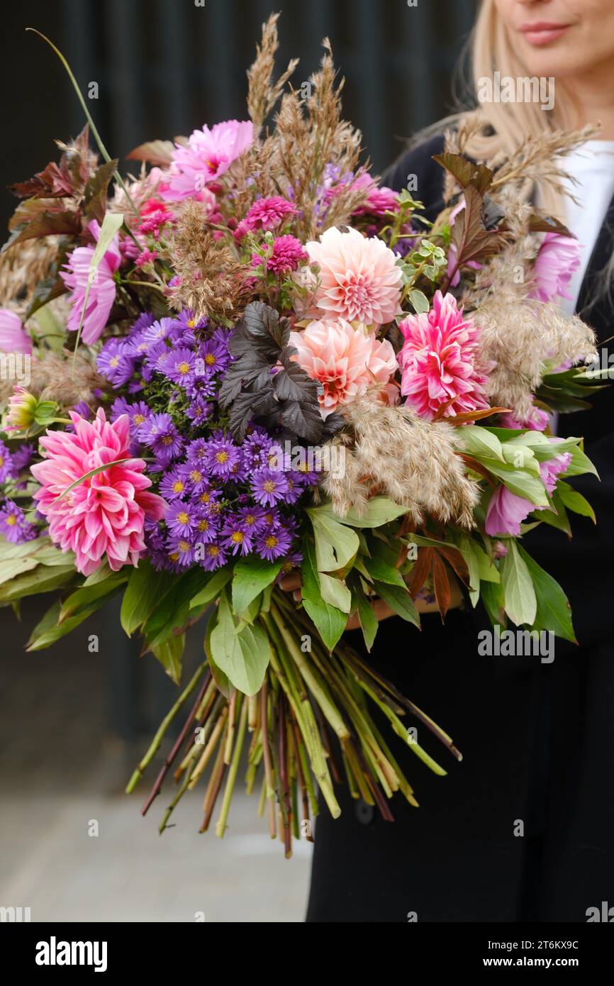 Un grande bouquet di fiori misti nelle mani di una donna. Il lavoro di un fiorista in un negozio di fiori. Foto Stock