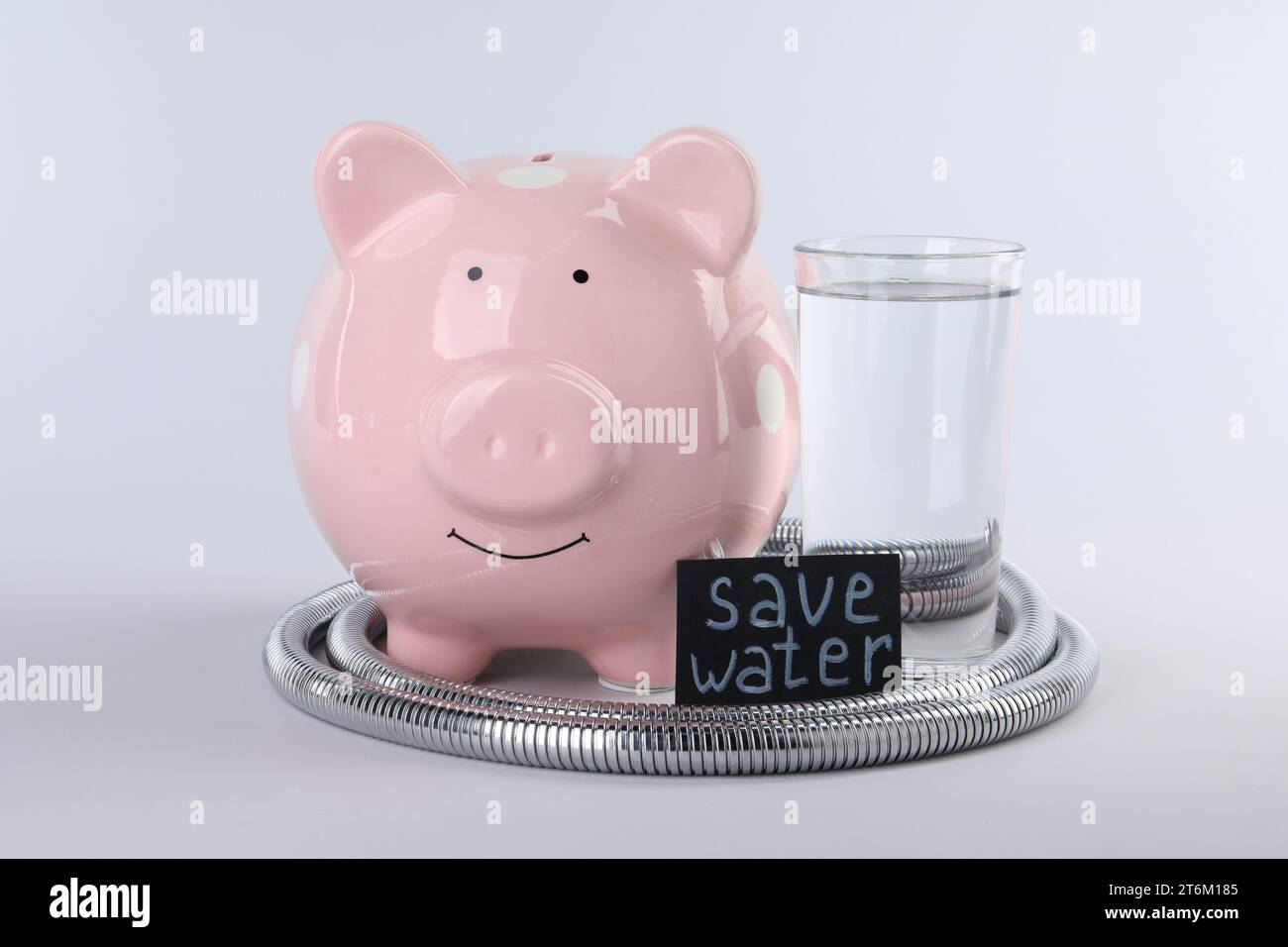 Concetto di scarsità d'acqua. Scheda con frase Save Water, salvadanaio, tubo doccia e bicchiere di bevanda isolato su bianco Foto Stock