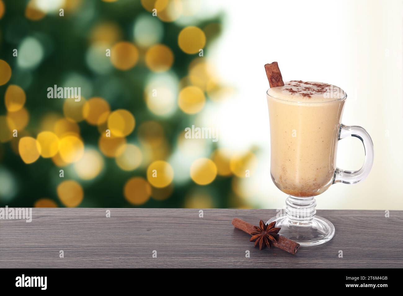 Delizioso eggnog in vetro su un tavolo di legno contro l'albero di Natale sfocato, spazio per il testo Foto Stock