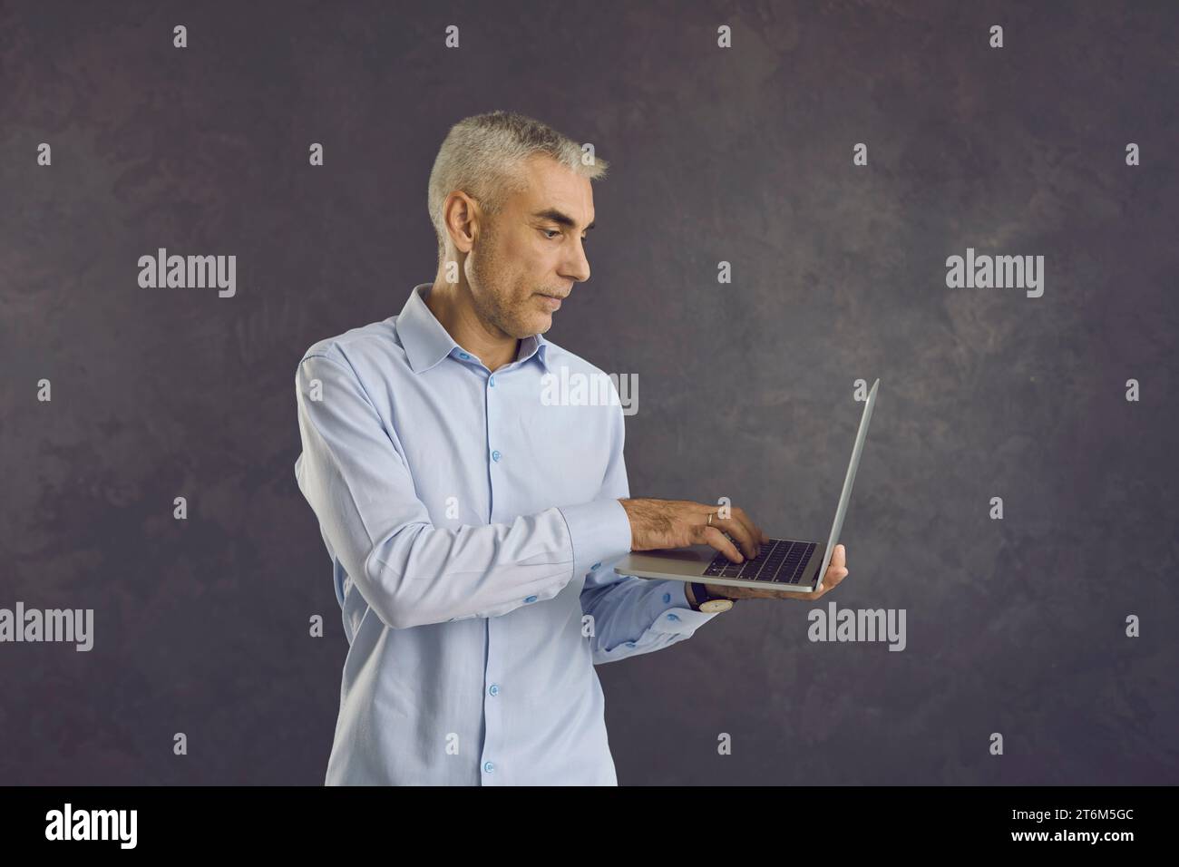 Foto in studio di un uomo anziano serio che tiene in braccio e usa il suo moderno computer portatile Foto Stock