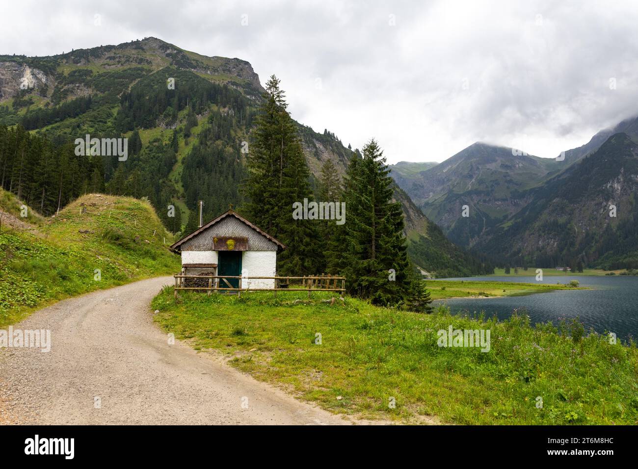 piccolo rifugio e sentiero di ghiaia sul lago di montagna nelle alpi austriache con montagne boscose sullo sfondo Foto Stock