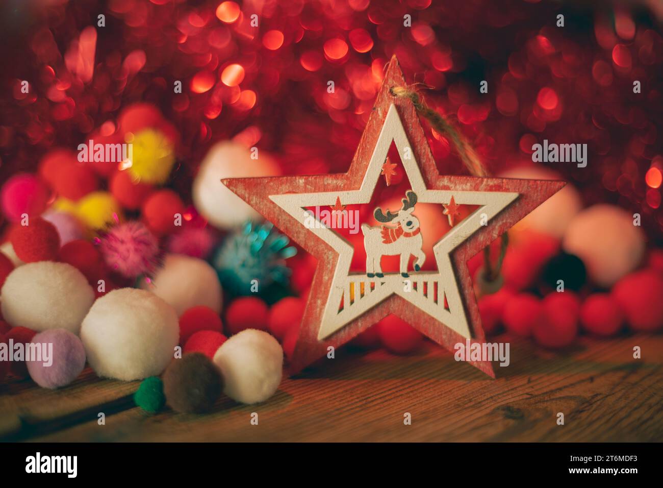 Ornamento natalizio in legno a forma di stella con una renna all'interno circondata da elementi e luci natalizie in tonalità rosse Foto Stock
