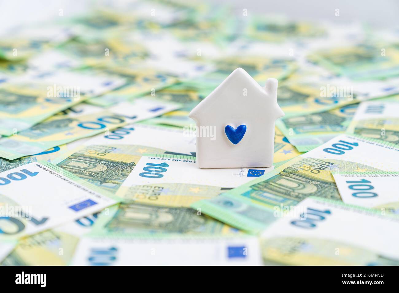Una piccola casa bianca con un cuore blu su molte banconote in euro, concetto di mutuo, pensione, risparmio, giovani abitazioni familiari Foto Stock
