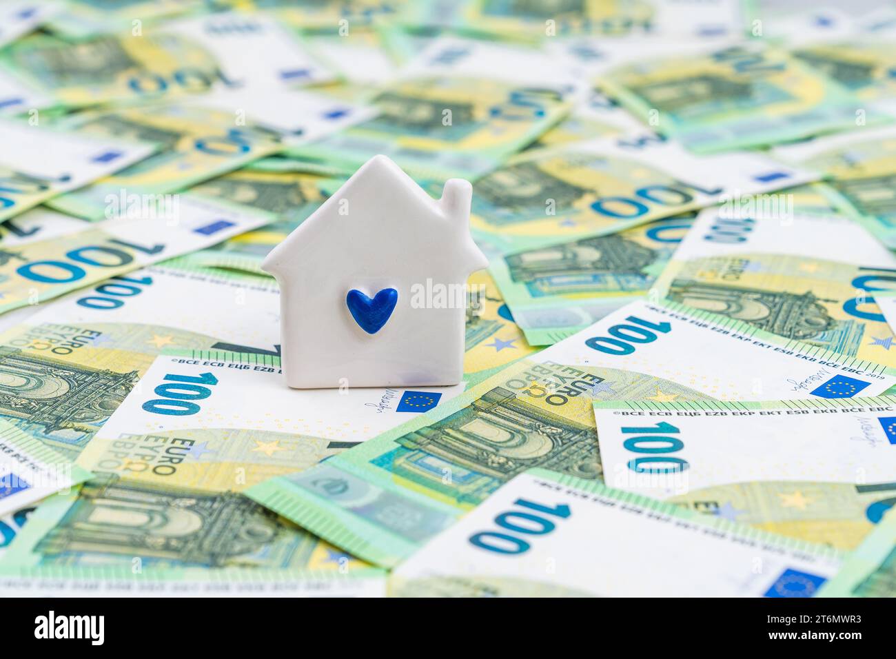 Vista frontale su una piccola casa bianca con un cuore blu su molte banconote, concetto di piano pensionistico. Foto di alta qualità Foto Stock