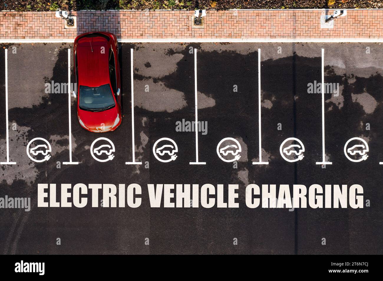 Vista aerea direttamente sopra una stazione di ricarica per veicoli elettrici con posti auto e segnaletica stradale che indica i vani di ricarica per auto elettriche Foto Stock